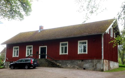 Kungslena församlingshem sett från vägen på andra sidan från kyrkan, en bil står parkerad framför församlingshemmet.