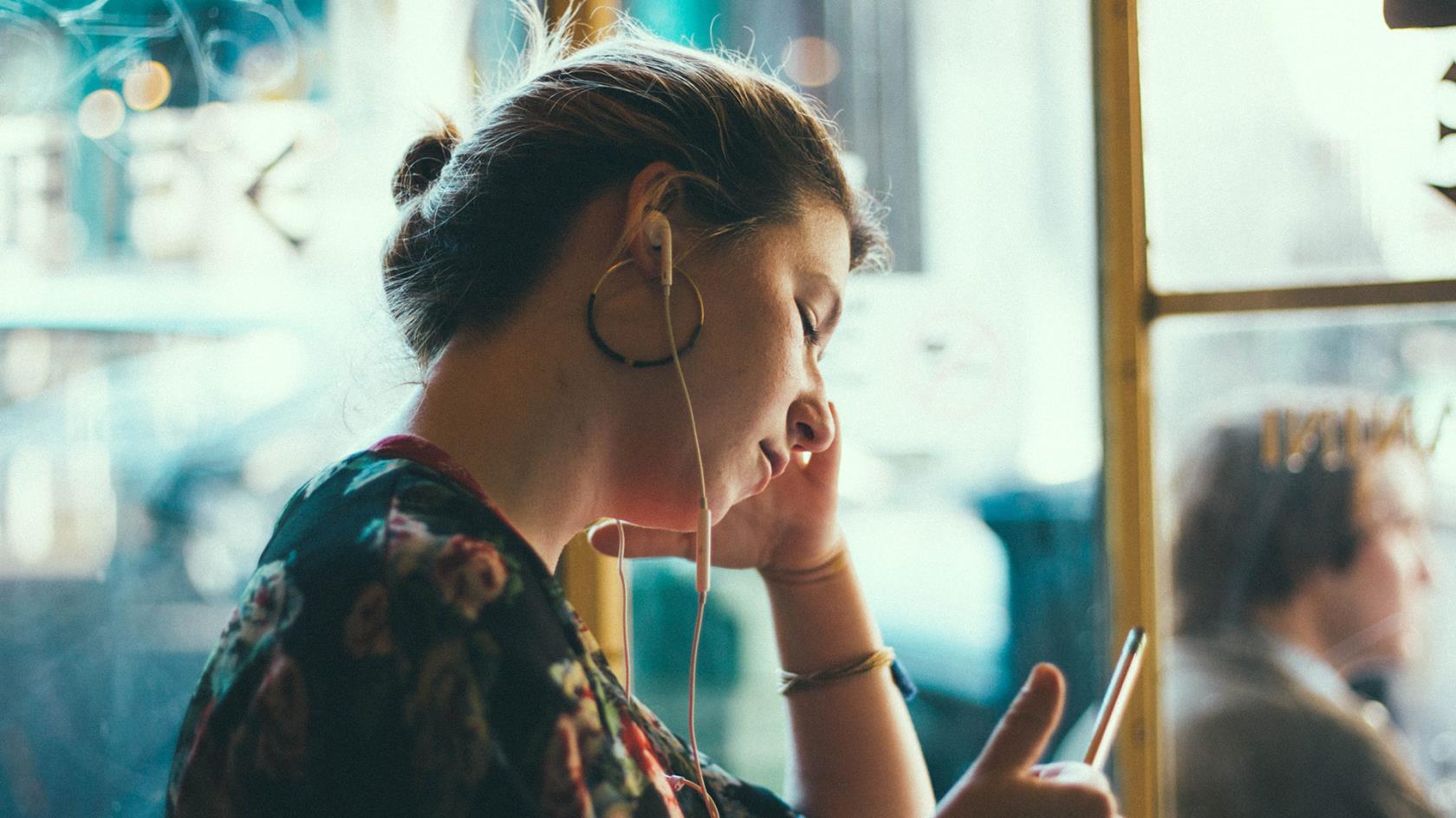 Kvinna som lyssnar i hörlurar och tittar på en mobiltelefon.