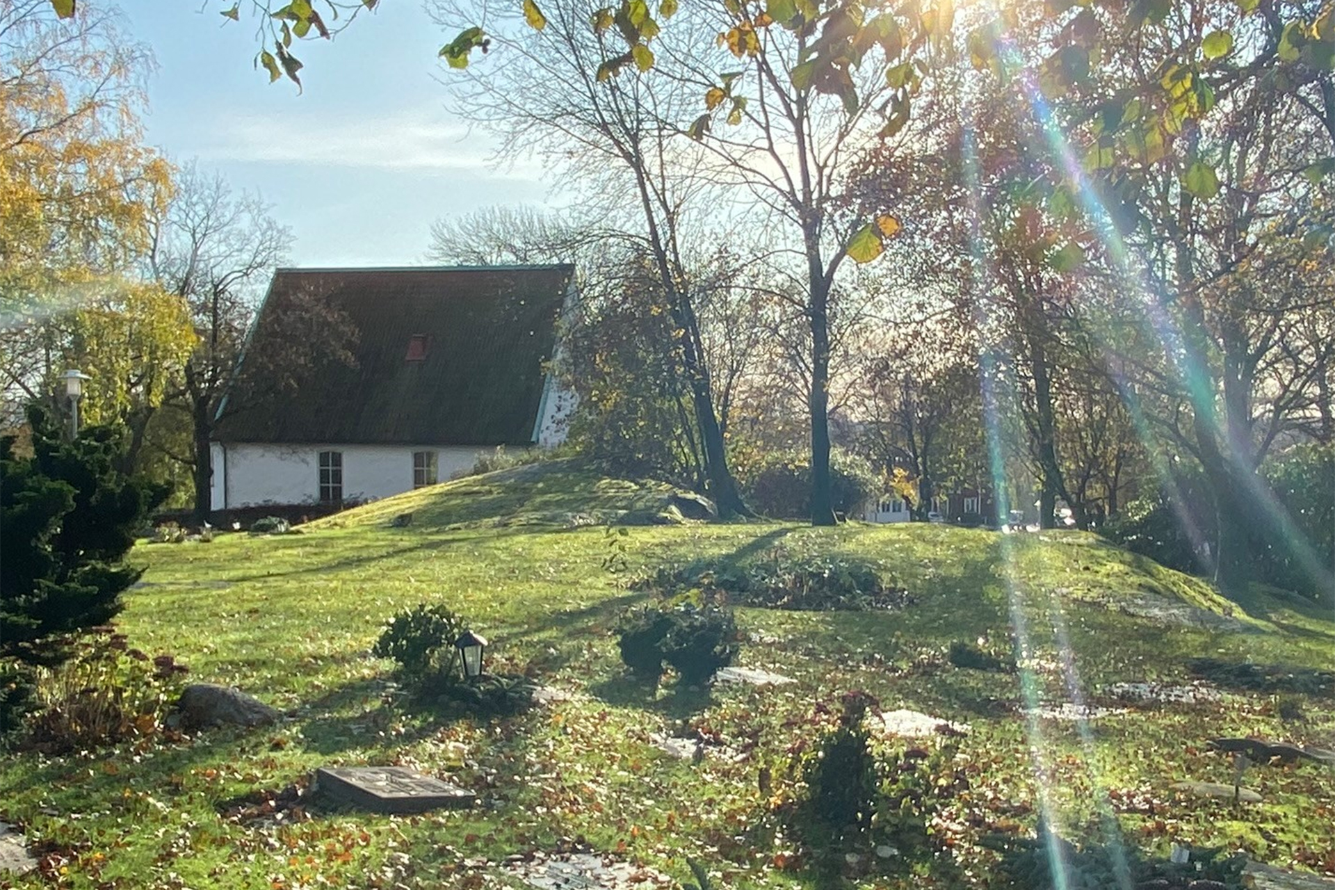 Lundby Gamla Kyrka i bakgrunden, kyrkogården i förgrunden. Solen lyser. 
