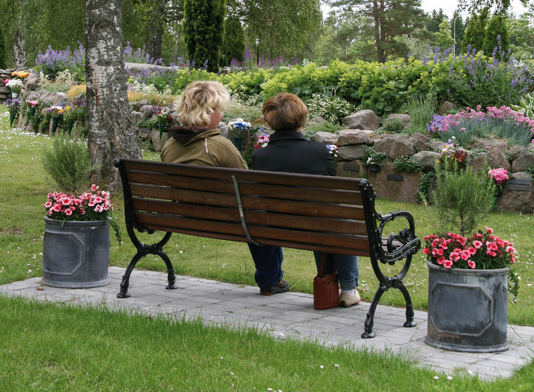 Två personer som sitter på en parkbänkssamtal på Norra kyrkogården i Tidaholm och samtalar med varandra.