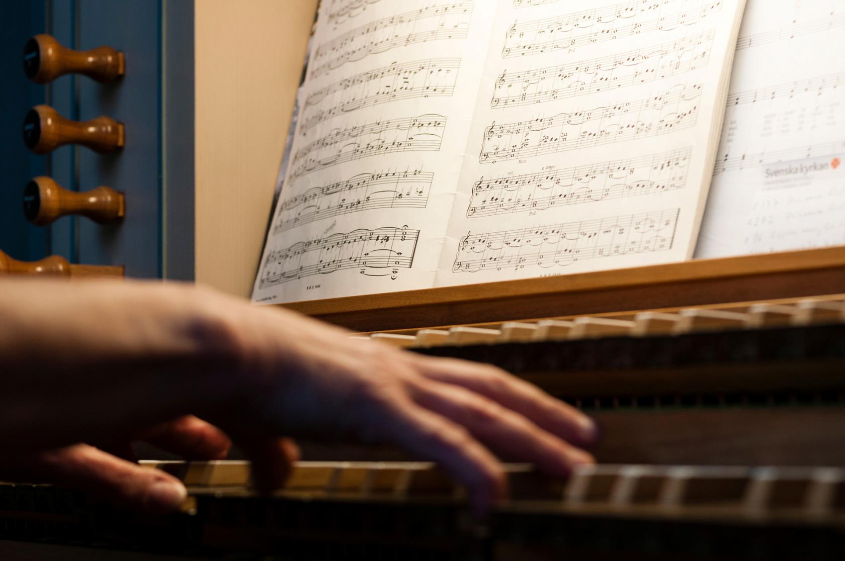 Händer som spelar på en orgel. i bakgrunden ses noter.