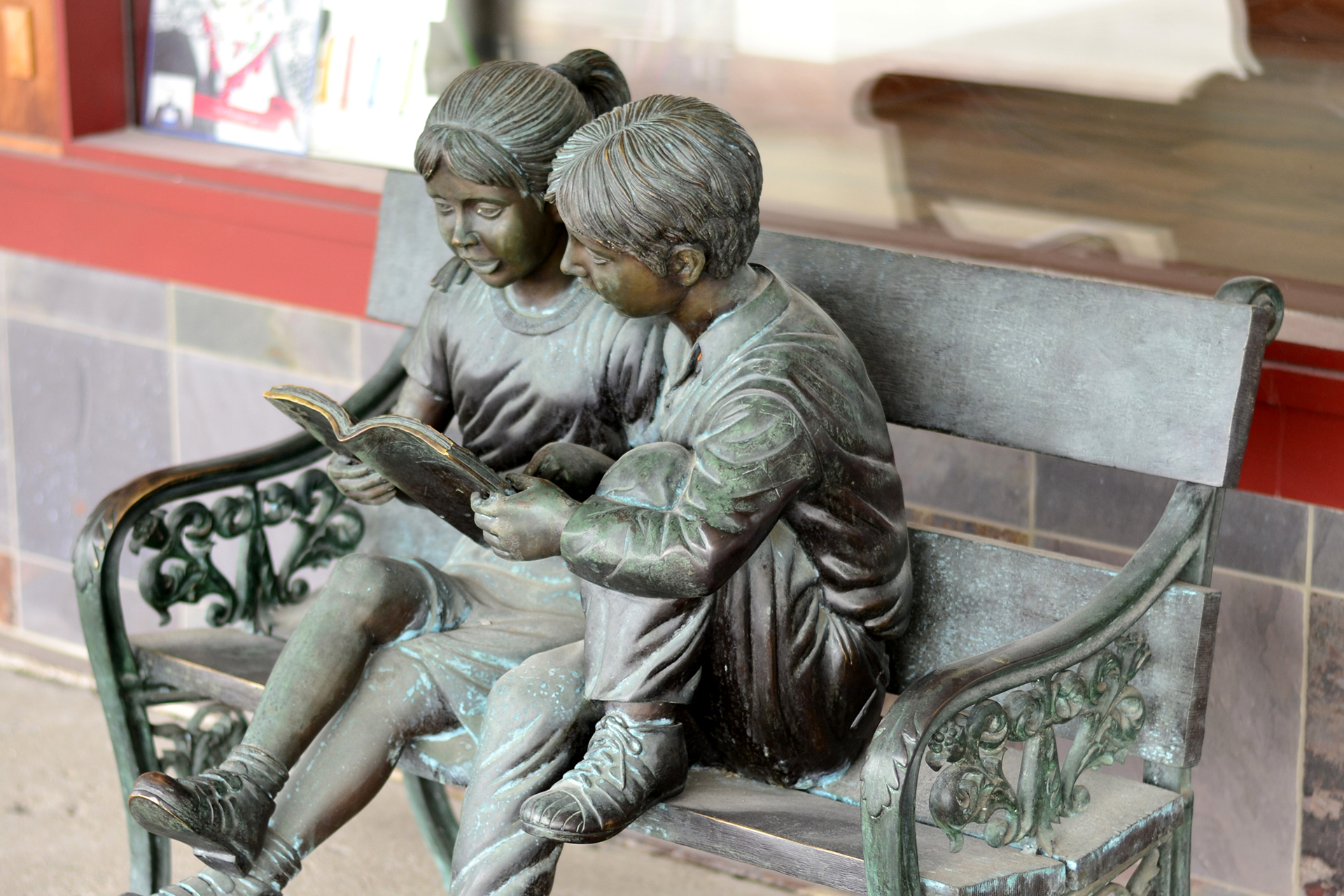 Staty av pojke och flicka som läser tillsammans på en parkbänk.