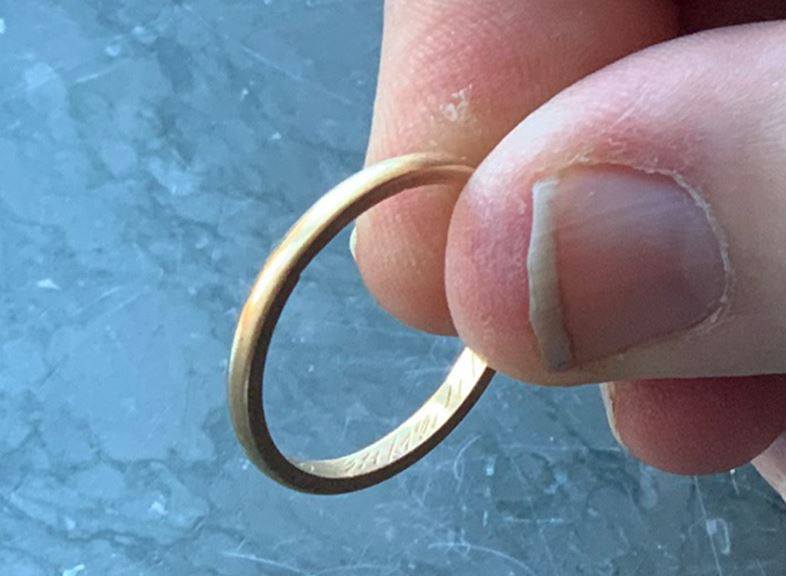 Vigselring i guld hållen i ett tumgrepp.