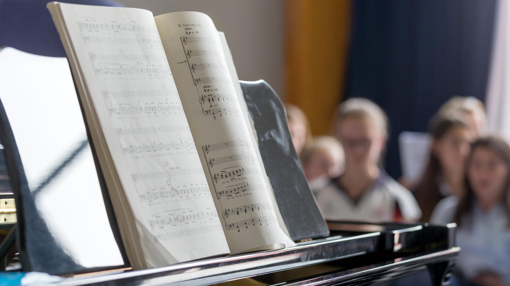 En orgel/ett piano och ett nothäfte, några människor i bakgrunden. 