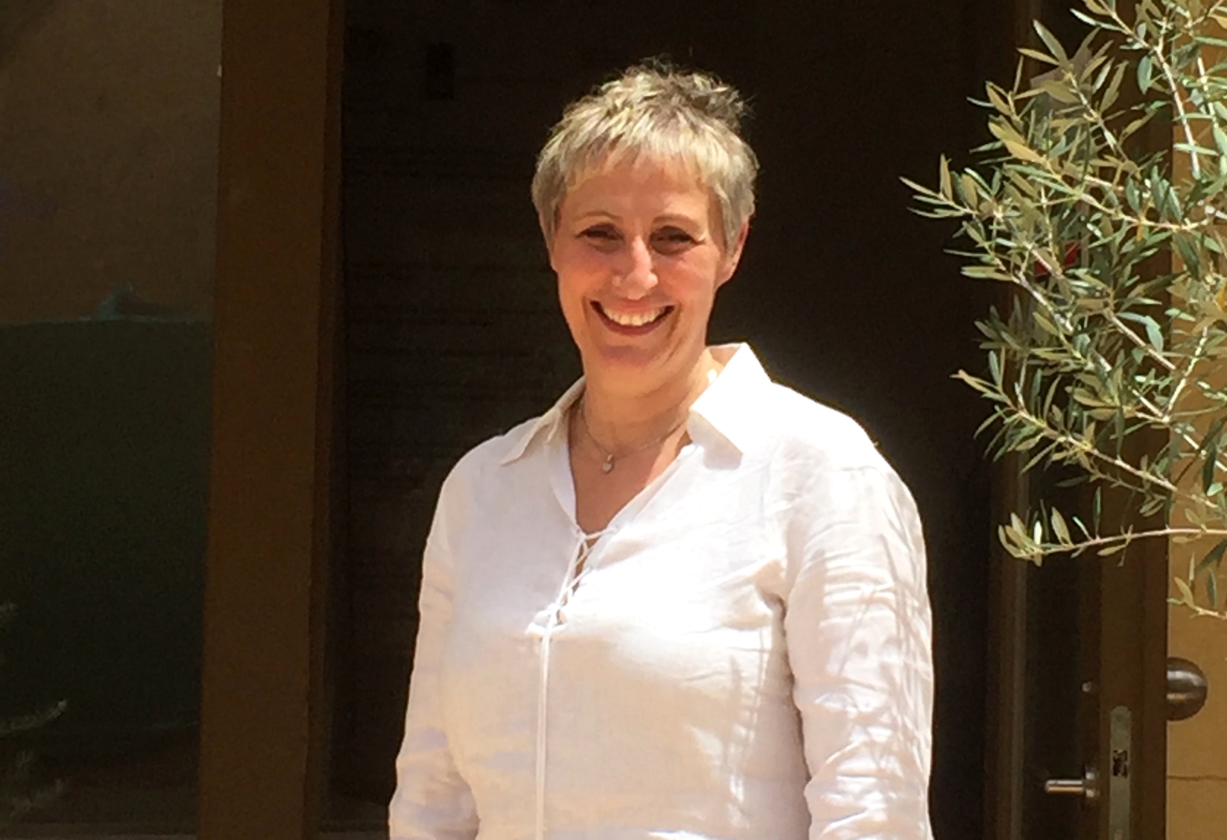 Kvinna i vit blus ler mot kameran. 