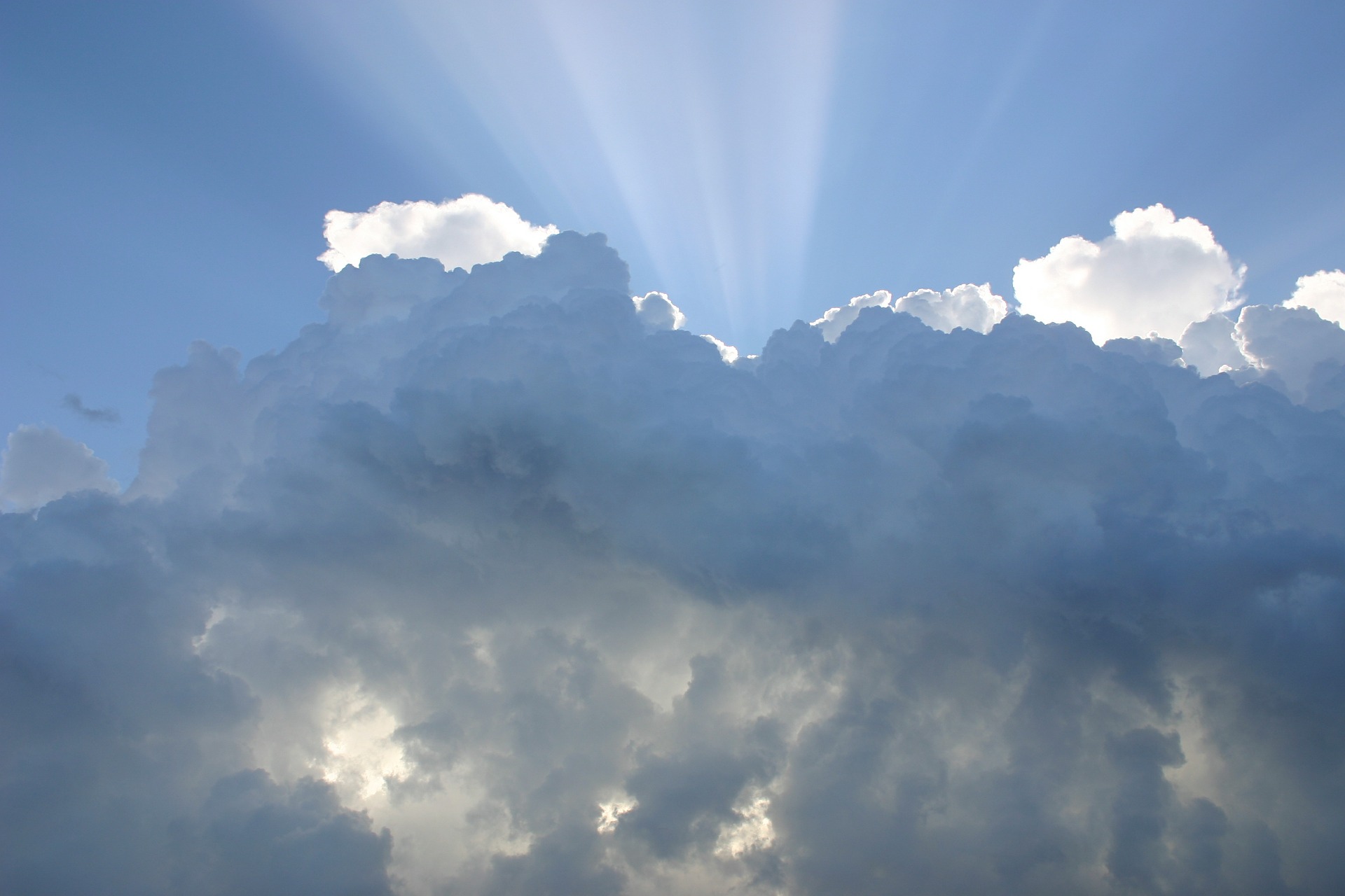 Moln och en blå himmel och solen lyser genom molnen uppåt.