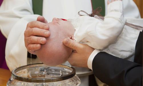 En prästs händer med vatten läggs på ett litet barns huvud.