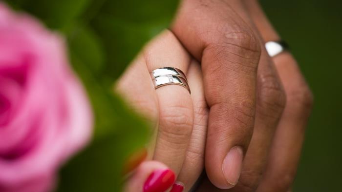 Vigselringar i silver på ett gift pars händer som håller hand.