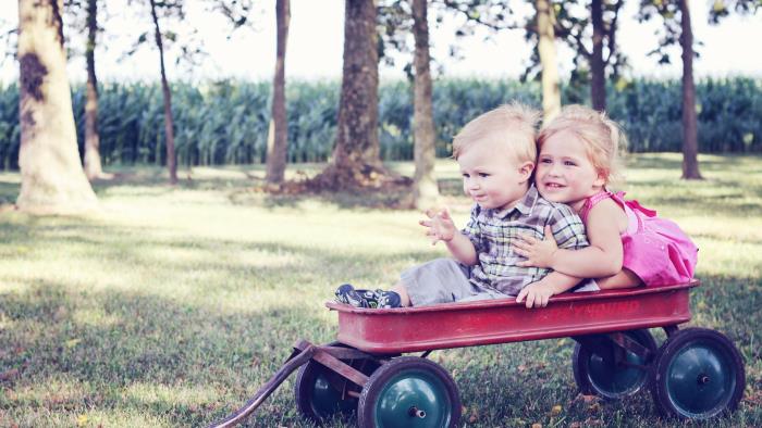 En liten pojke och en liten flicka sitter på en kärra och är glada
