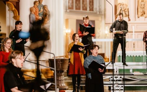 Åtta körsångare står och sjunger på coronasäkert avstånd från varandra i Umeå stads kyrka.