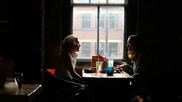 Två kvinnor sitter vid ett bord vid ett fönster och samtalar.