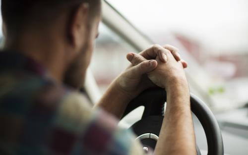 En man sitter i bilen med händerna knäppta på ratten.