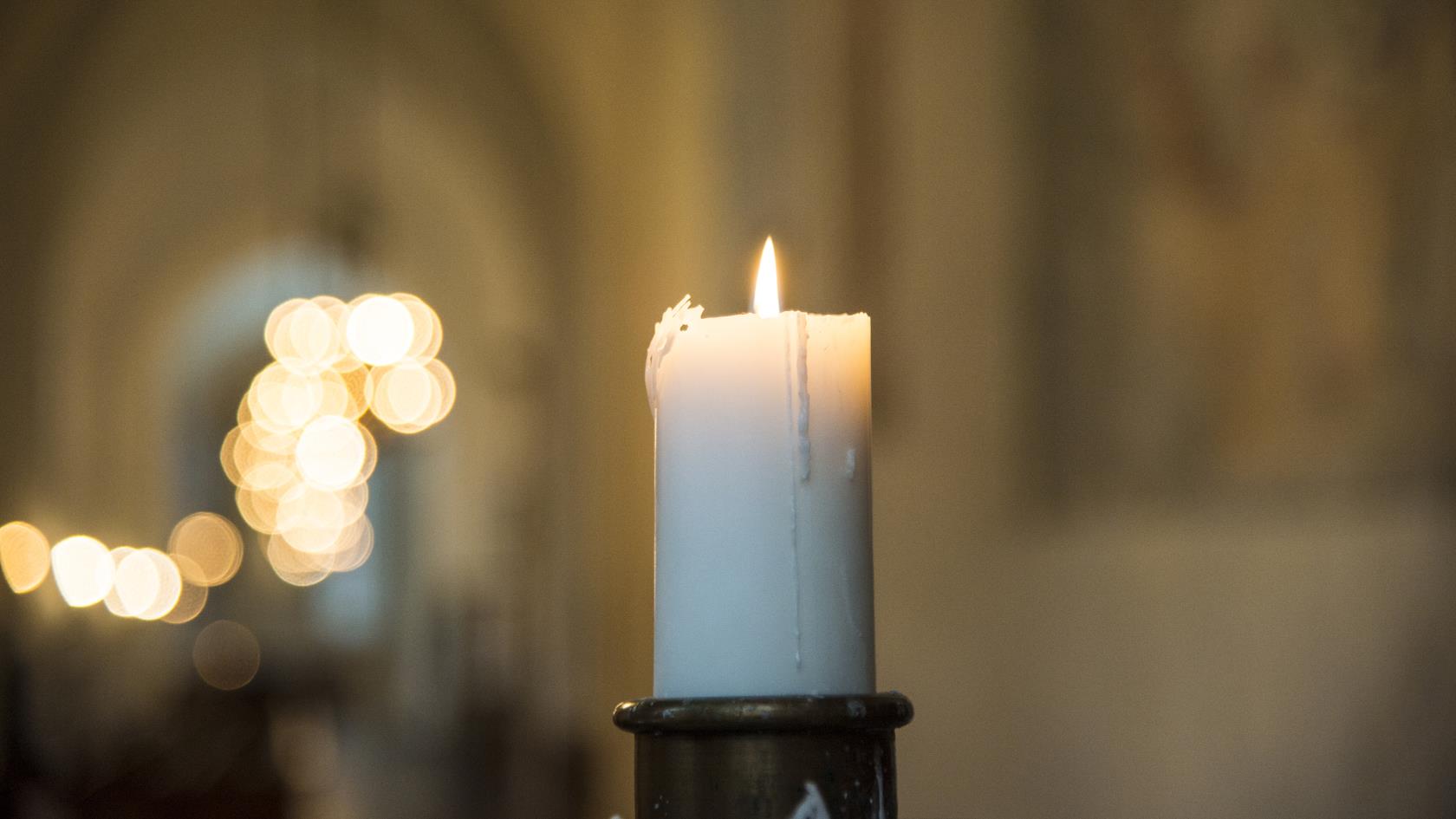 Ett tänt stearinljus i en kyrka.